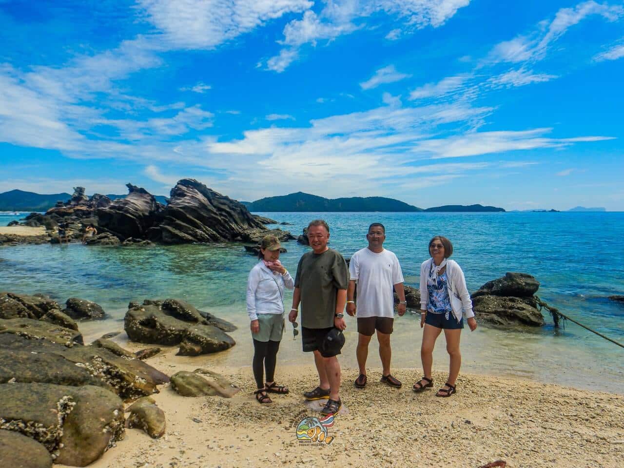カイ島の岩場と海を背景に撮影する4名のお客様