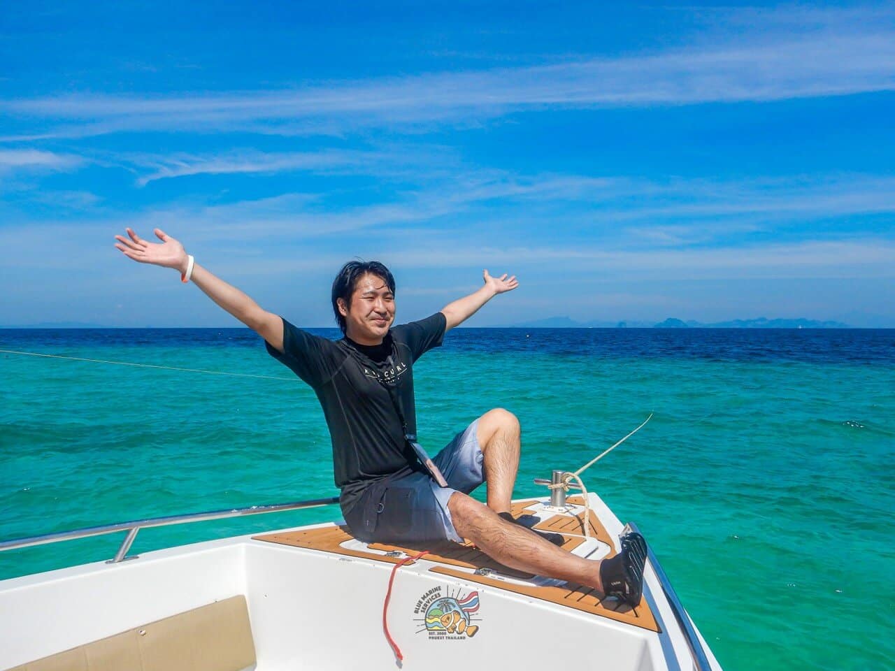 青い海を背景にスピードボートの船首で両手を広げるお客様